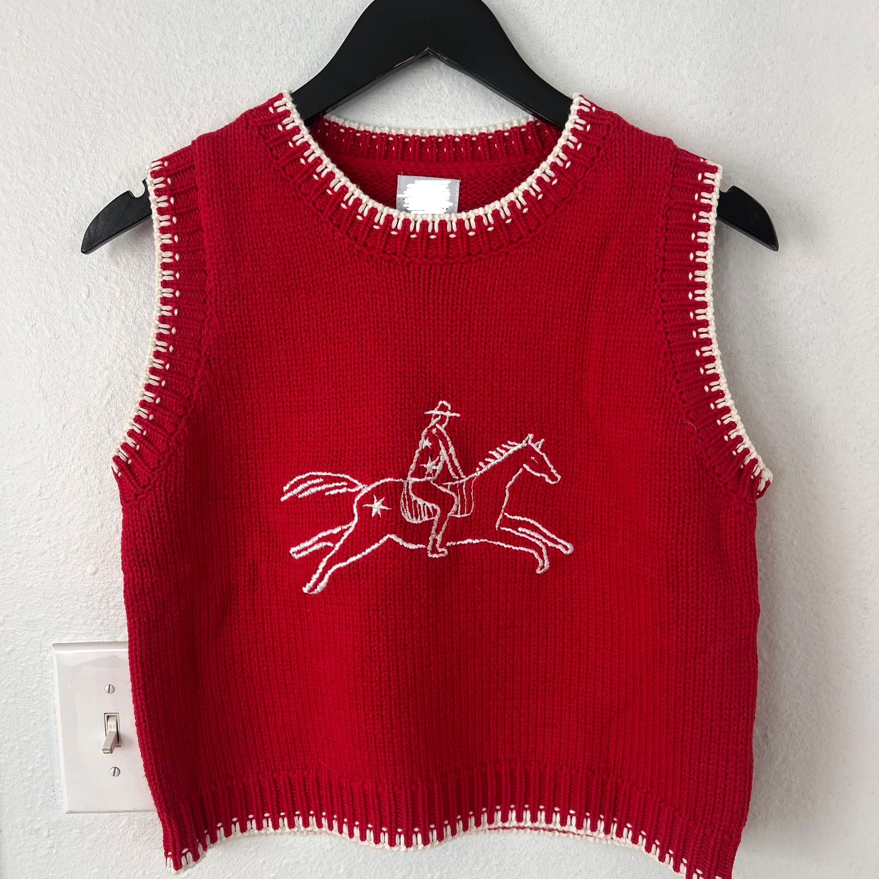 Red knitted sweater vest with white embroidered horse and rider design and whipstitch trim